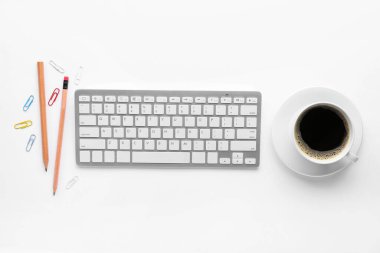 Modern bilgisayar klavyesi, beyaz arka planda bir fincan kahve ve kırtasiye malzemesi.