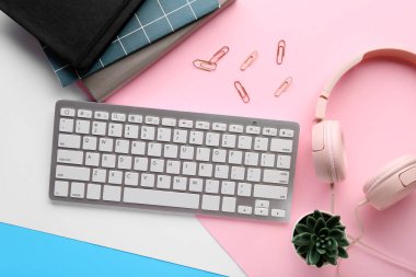 Modern bilgisayar klavyesi, kulaklıklar, ev bitkisi, not defterleri ve renkli arkaplan üzerine ataçlarla kompozisyon