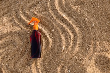 Deniz sahilinde kumsalda bir şişe güneş kremi.