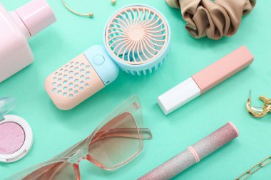 Portatif elektrikli vantilatör ve turkuaz arka planda kadın aksesuarları olan kompozisyon