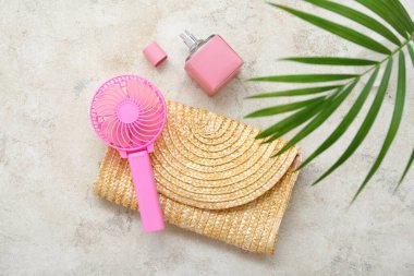 Portatif pembe elektrikli vantilatör, hasır çanta, parfüm ve gri grunge arka planda palmiye yaprakları.