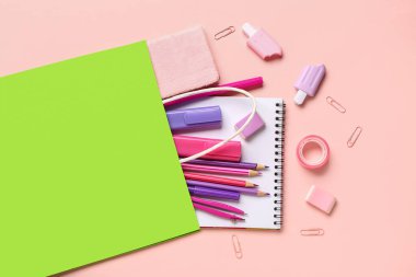 Pembe arka planda farklı okul kırtasiyesi olan yeşil alışveriş çantası.