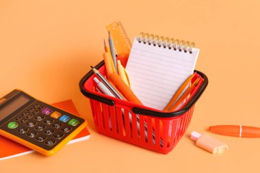 Turuncu arka planda farklı okul kırtasiyesi olan alışveriş sepeti, yakın plan.