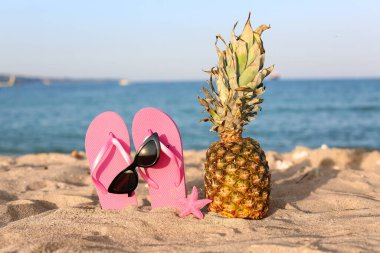 Deniz kıyısında terlikli, deniz yıldızı ve ananaslı şık güneş gözlükleri.