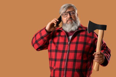 Elinde baltayla bej arka planda telefonla konuşan olgun oduncunun portresi.