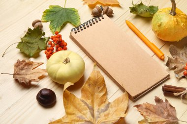 Kahverengi ahşap arka planda defter, balkabağı ve sonbahar yapraklarıyla kompozisyon