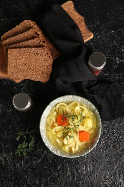 Bowl of tasty chicken soup and bread on black background