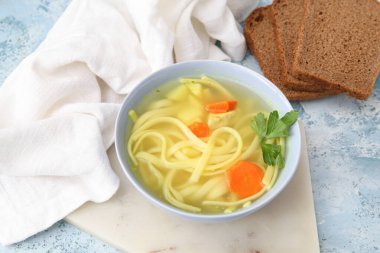 Mavi arka planda bir kase lezzetli tavuk çorbası ve ekmek.