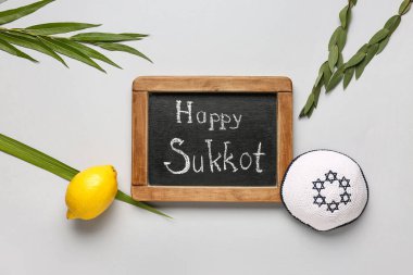 Dört tür (lulav, hadas, arava, etrog) ve gri arkaplanda Mutlu SUKKKOT yazılı kara tahta