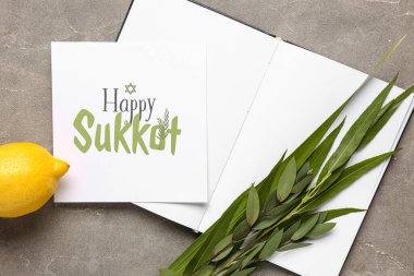 Dört tür (lulav, hadas, arava, etrog), gri grunge arkaplan üzerinde Mutlu SUKKOT yazılı açık kitap ve tebrik kartı