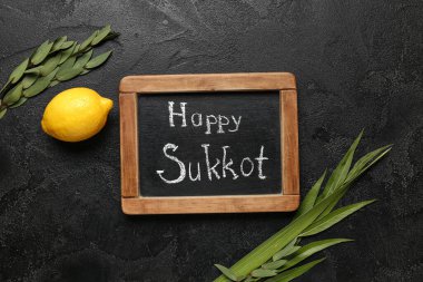 Dört tür (lulav, hadas, arava, etrog) ve siyah grunge arkaplan üzerinde HAPPY SUKKOT yazılı kara tahta