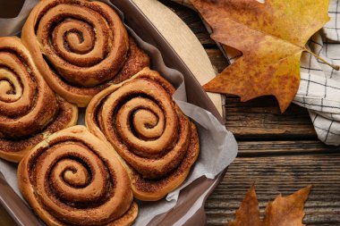 Ahşap zemin üzerinde lezzetli tarçın ruloları ve sonbahar yaprakları pişirme yemeği