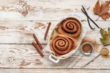 Beyaz ahşap arka planda lezzetli tarçınlı çörekler ve sonbahar yaprakları pişirmek.