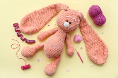 Örülmüş tavşan oyuncağı, iplik yumağı ve sarı arka planda şerit.