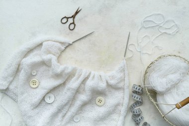 Beyaz arka planda örgü iğneleri, iplikler ve mezuralar.