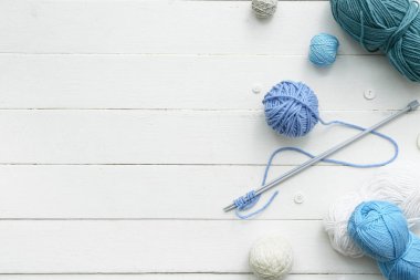 İplik topları, örgü iğneleri ve beyaz ahşap arka planda düğmeler