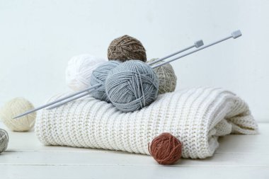 Beyaz ahşap masada örülmüş süveter, iğneler ve iplik topları