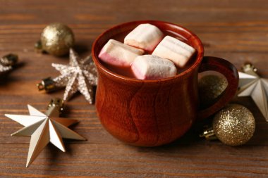 Marşmelovlu bir fincan sıcak çikolata ve ahşap arka planda Noel topları.