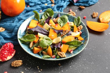 Bir tabak lezzetli salata, hurma, nar tohumu ve siyah arka planda ceviz.