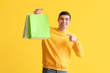 Sarı arka plandaki alışveriş çantalarını gösteren mutlu genç adam.