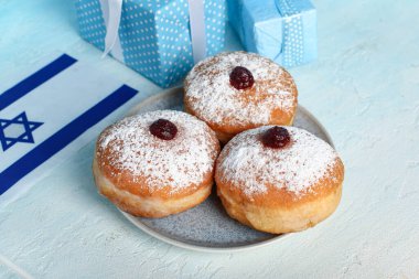 Hafif arka planda Hanuka kutlaması için İsrail bayrağı ve lezzetli çöreklerle dolu tabaklar.