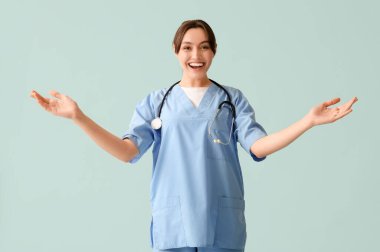 Güzel bayan doktor mavi arka planda el sallıyor.