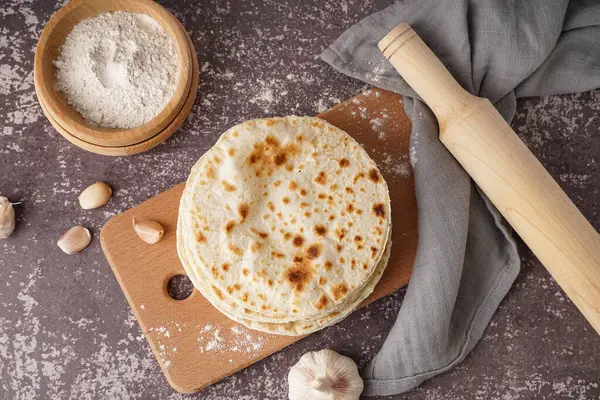 Gri arka planda tahtadan yapılmış lezzetli pide ekmeği ve unu var.