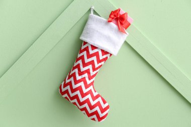 Yeşil arka planda hediye kutusuyla Noel çorabı asılı.