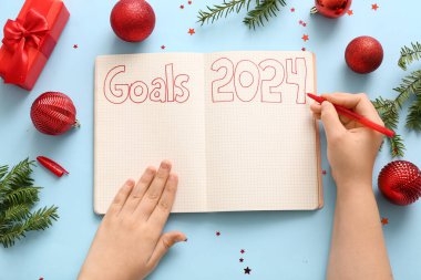 Not defterinde hedefler yazan kadın 2024 ve mavi arka planda Noel dekoru