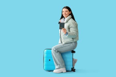 Pasaportu ve bileti olan genç bir kadın bavulun üzerinde oturuyor.