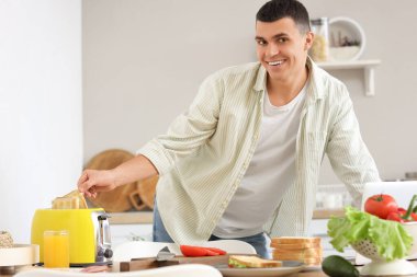 Genç adam mutfakta sandviçler için çıtır çıtır tost yapıyor.