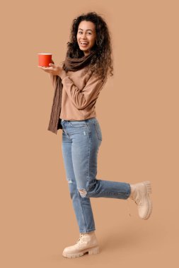 Kahverengi arka planda sıcak şarapla eşarplı mutlu Afro-Amerikalı kadın.