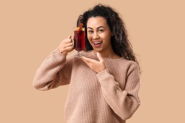 Kahverengi arka planda cam bardak sıcak sıcak şarapla güzel bir Afro-Amerikalı kadın.