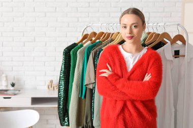 Stüdyoda duvarın yanındaki askıda giysileri olan mutlu kadın stilist.