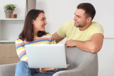 Taşınırken odada dizüstü bilgisayar kullanan mutlu genç çift.