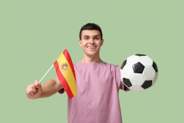 Yeşil arka planda futbol topu ve İspanya bayrağı olan genç bir adam.