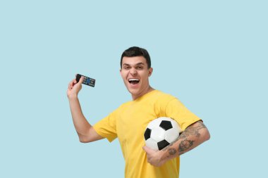 Mavi arka planda futbol topu ve uzaktan kumandalı genç adam.