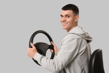 Dümeni gri arka planda sandalyede oturan mutlu genç adam.