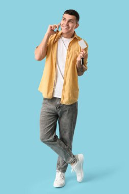 Boş ehliyeti olan genç adam mavi arka planda cep telefonuyla konuşuyor.