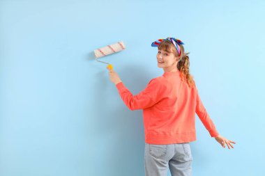 Mavi arka planda boya silindirli genç bir kadın. Onarım kavramı