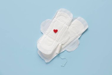 Kırmızı kalbi ve mavi arka planda tamponu olan adet pedleri.