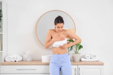 Güzel bir kadın banyoda göğüslerini kontrol ediyor. Kanser farkındalığı kavramı