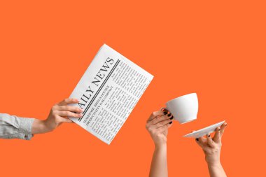 Gazete ve turuncu arka planda bir fincan kahveli kadın eli.