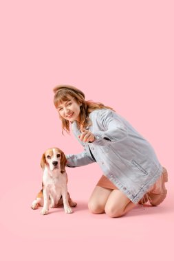 Gayri resmi giyinmiş genç bir kadın ve sevimli bir av köpeği pembe arka plandaki izleyiciyi işaret ediyor.