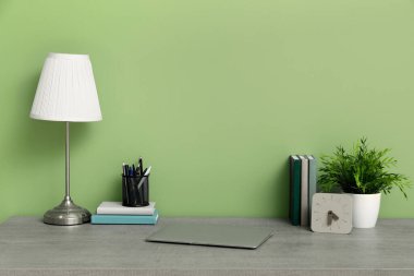 Yeşil duvarın yanında lamba ve dizüstü bilgisayarı olan şık bir iş yeri