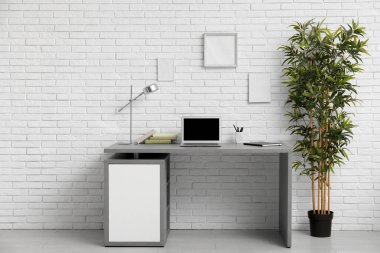 Beyaz duvarın yanında ev bitkisi ve masa olan modern bir iş yeri