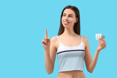 Vajinal fitilleri mavi arka plandaki bir şeyi gösteren güzel bir genç kadın.