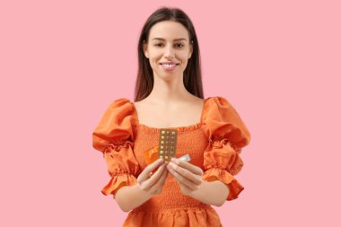 Doğum kontrol hapları, vajinal fitiller ve pembe arka planda prezervatifi olan güzel bir kadın.