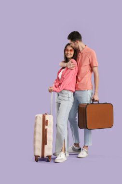 Güzel, genç, mutlu, mor arka planda bavulları olan turistler.