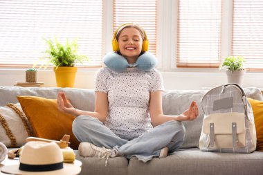 Kulaklıklı genç hamile kadın evdeki kanepede meditasyon yapmaya hazır.